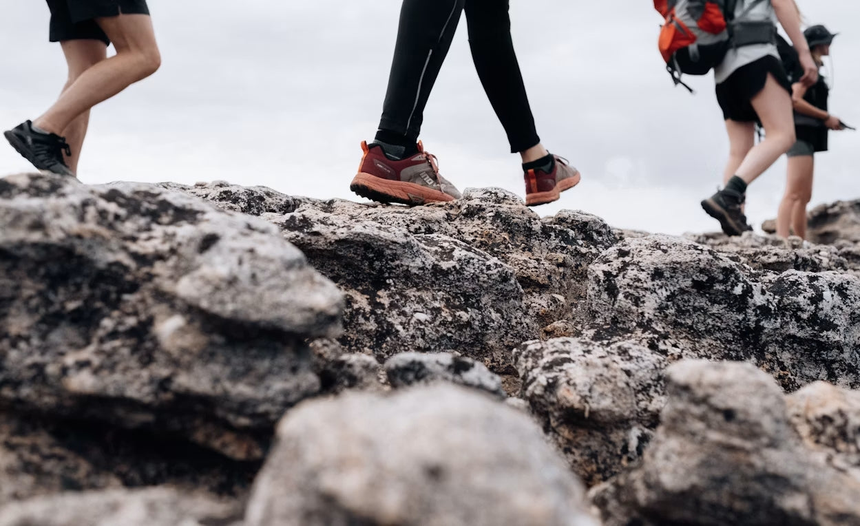 Hiking boots and trail runners side by side on a forest hiking trail